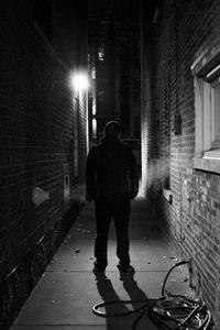 Rear view of man standing in illuminated alley at night