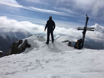 Rear view of man standing on snowcapped mountain against sky