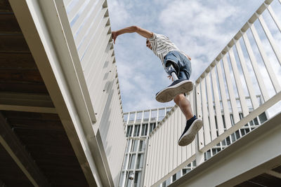 Low angle view of man with artificial limb jumping amidst bridge railing in city