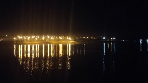 Illuminated city by river against sky at night