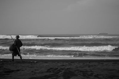 Rear view of man standing on beach against clear sky