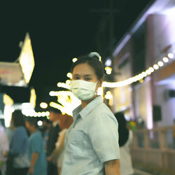 Asian women wearing masks go   event that is held at night. it is decorated with many light bulbs.