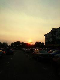 Cars on road by buildings against sky during sunset