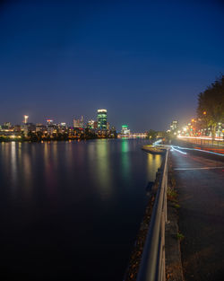 Illuminated city by river against sky at night