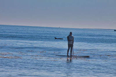 Rear view of man standing on beach against clear sky