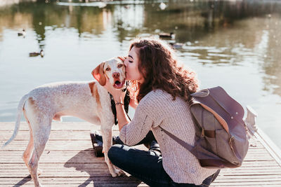 Woman with dog kissing on pier over lake