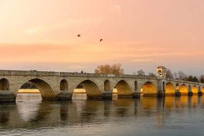 Arch bridge over river against sky during sunset