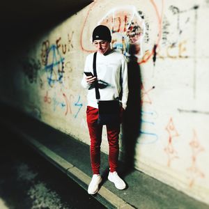 Full length portrait of young man standing against graffiti wall