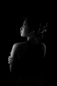 Side view of young woman looking away against black background