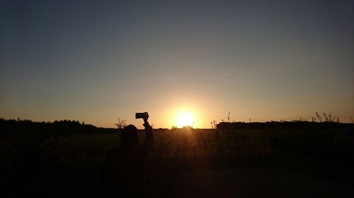 Silhouette of person photographing at sunset