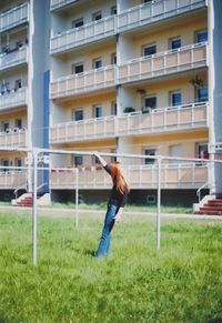 Full length of woman leaning on metallic pole against building