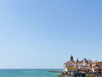 Buildings by sea against clear blue sky