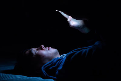 Close-up of man using phone while lying on bed in darkroom