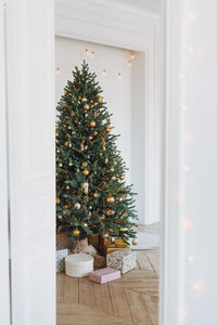 Decorated christmas tree in golden and white toys with the gift boxes from door at bright interior