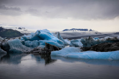 Icebergs melting in lagoon against cloudy sky