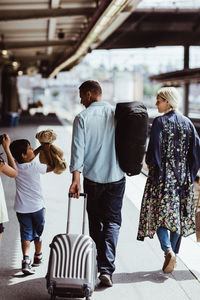 Rear view of man holding luggage while walking with family at railroad station