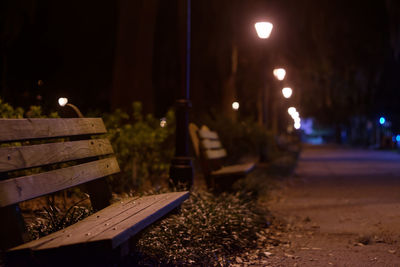 Empty benches by illuminated street lamps on footpath