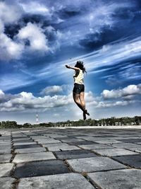 Full length of woman jumping in mid-air over cobbled street against sky