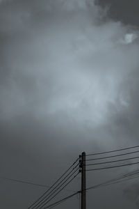 Low angle view of electricity pylon against cloudy sky