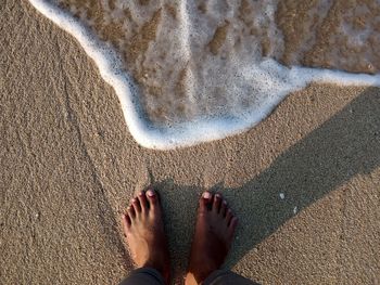 Low section of man standing at sea shore