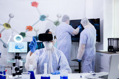 Scientist wearing virtual reality simulator colleague in background at laboratory