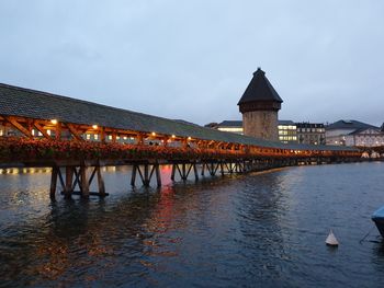 Bridge over river by illuminated building against sky