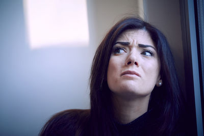 Close-up of worried woman looking away by window