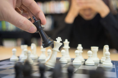 Cropped hand of man playing chess with female friend on table in library