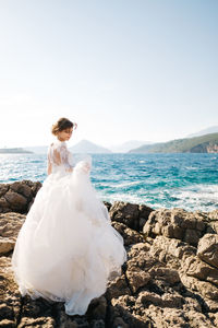 Rear view of woman on rock at beach against sky