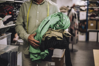 Midsection of male fashion designer holding clothes at workshop