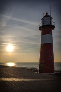 Lighthouse by sea against sky during sunset