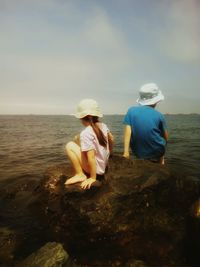 Rear view of boys sitting on shore against sky