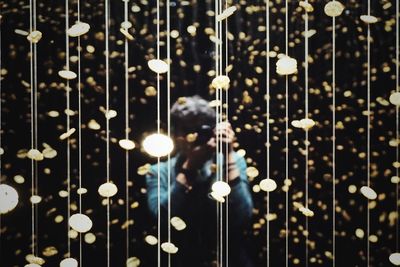 Woman photographing while standing amidst illuminated lights at night