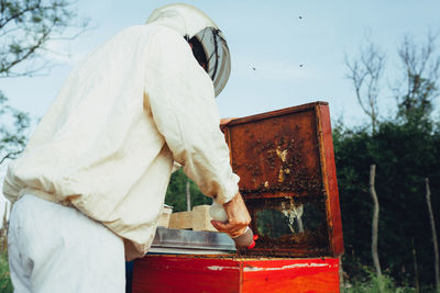 Side view of beekeeper examining beehive on land