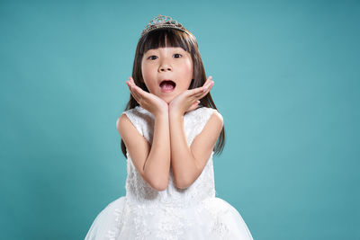 Portrait of girl wearing crown while standing against turquoise background