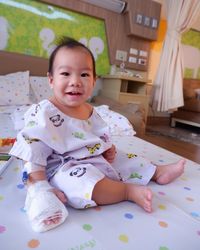 Portrait of cute baby boy wearing iv drip while sitting on bed at home