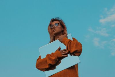 Low angle view of woman holding mirror against blue sky