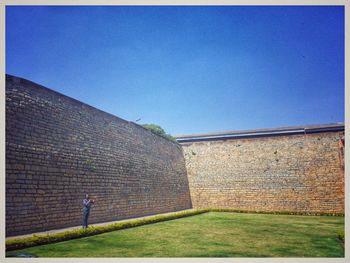 Man standing on brick wall against blue sky