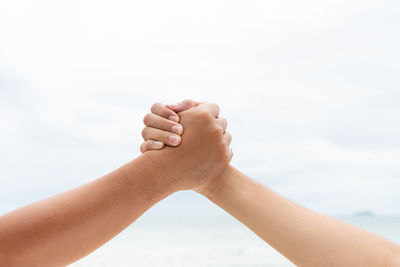 Close-up of people holding hand against sky