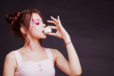 Beautiful young woman with make-up holding sweet food against gray background