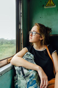 Young woman looking away while sitting on window