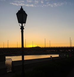 Silhouette bridge by river against clear sky during sunset