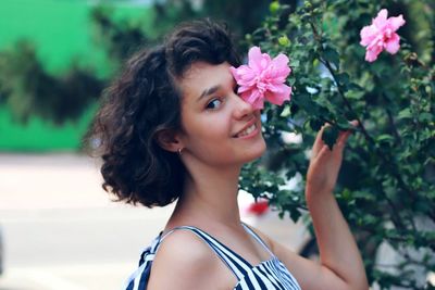 Portrait of smiling woman holding pink flower on plant