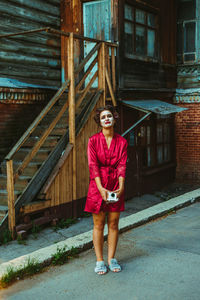 Portrait of young woman standing against building
