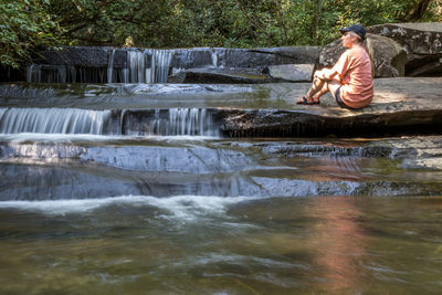 Full length of young woman sitting by waterfall