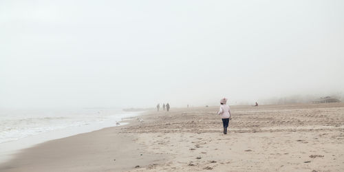 Young girl is playing on an empty beach during a foggy, cold day