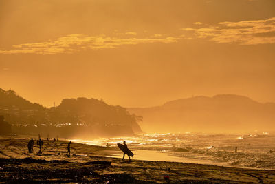 Silhouette people on beach against sky during sunrise