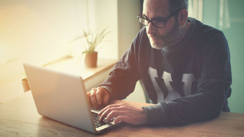 Man using laptop on table by window