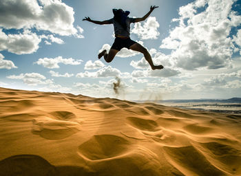 Full length of man jumping on sand in desert against sky