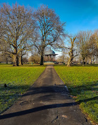 Footpath by bare trees on field against sky